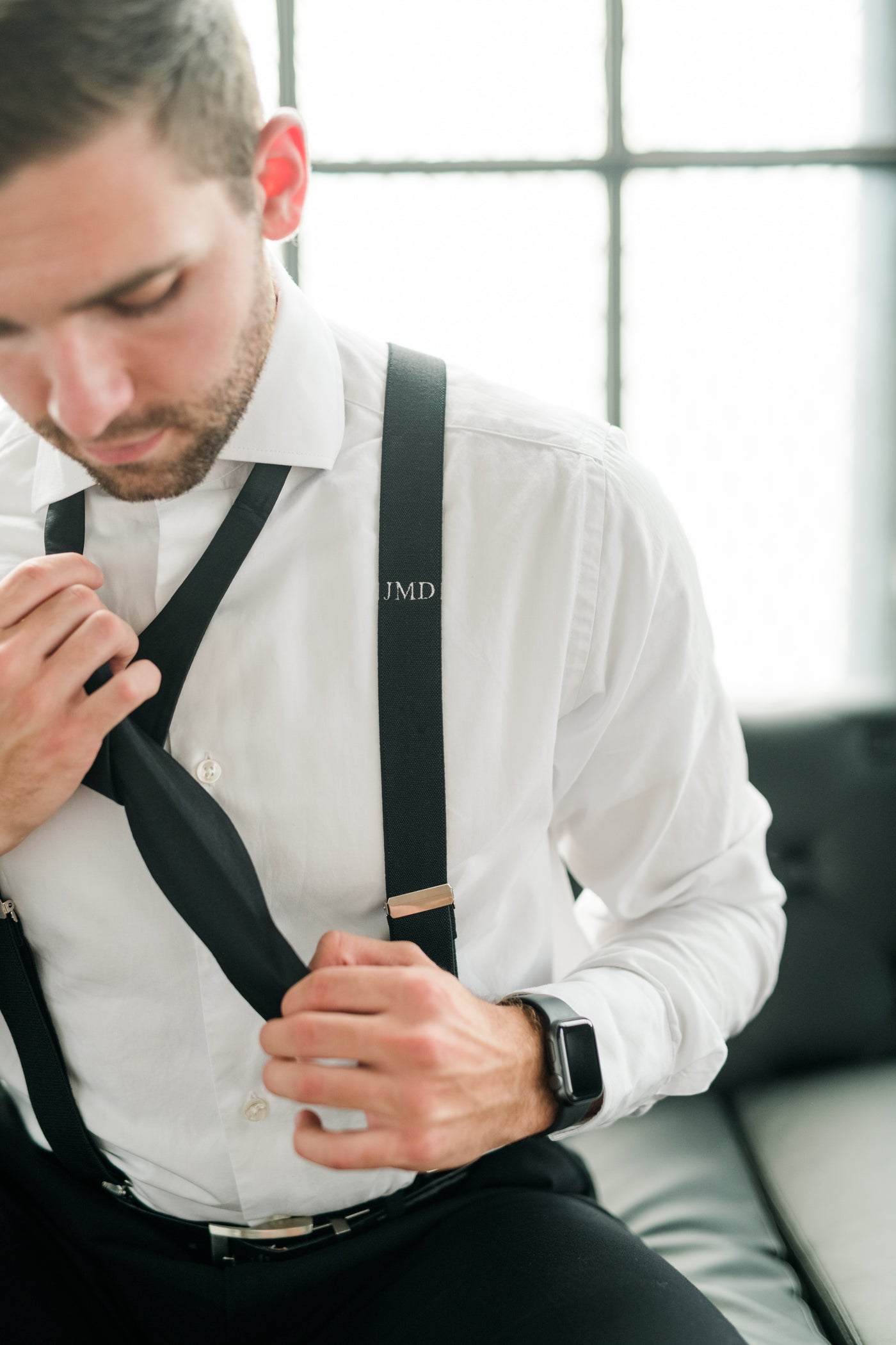 groom tying black silk bow tie with monogram suspender