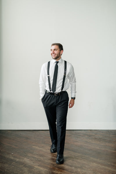 groom walking wearing monogram suspender and black dress pants for wedding