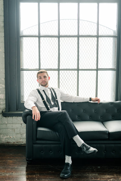 man sitting on couch wearing black bow tie and black suspender