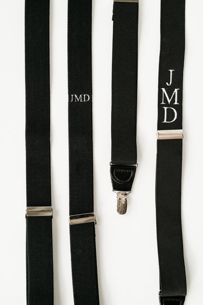 monogram suspenders laying flat one with horizontal embroidery and one with vertical embroidery
