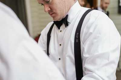 black tie wedding with groom helping groomsmen clip on his monogram suspender