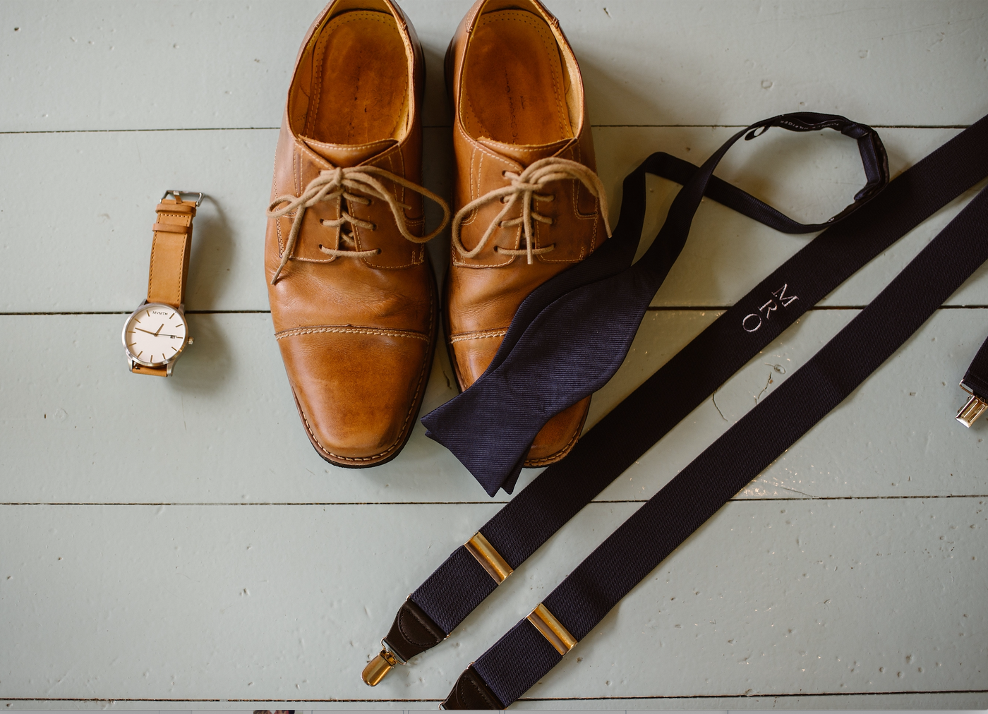 wedding flat lay with monogram suspender, dress shoes, watch, black bow tie